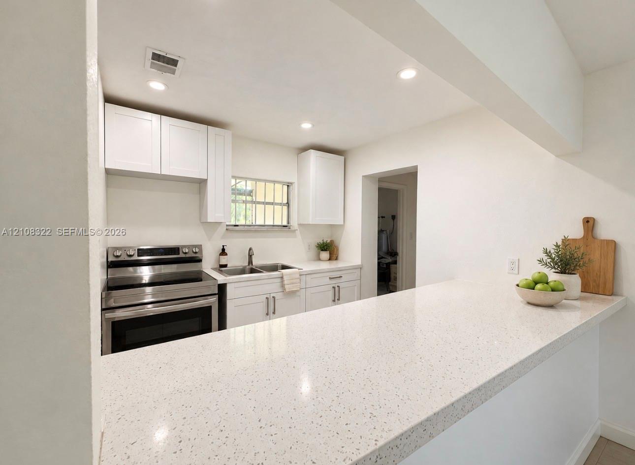 Kitchen featuring white shaker-style cabinetry, a quartz countertop breakfast bar, recessed lighting, and stainless steel appliances