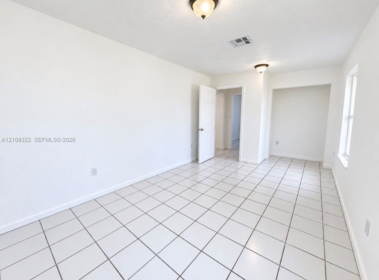 Room featuring white ceramic tile flooring, recessed wall niche, two flush-mount light fixtures, and a six-panel door