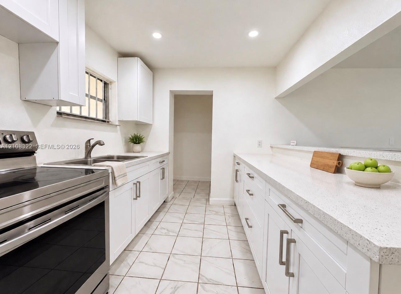Kitchen featuring white shaker-style cabinetry, light-toned stone countertops, stainless steel range, and tile flooring