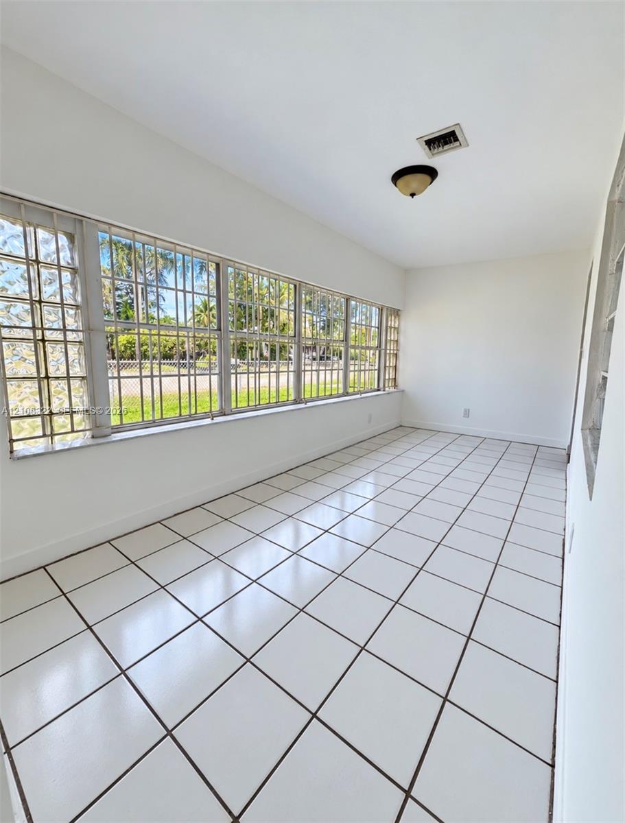 Enclosed space featuring square ceramic tile flooring, an expansive wall of multi-pane windows with metal security bars, glass block side accents, and a flush-mount ceiling light fixture Enclosed space featuring square ceramic tile flooring, an expansive wall of multi-pane windows with metal security bars, glass block side accents, and a flush-mount ceiling light fixture