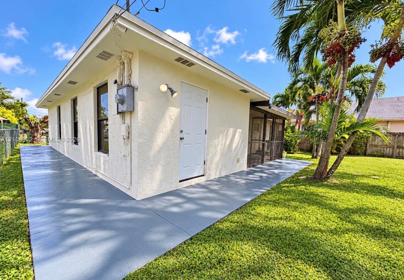 Stucco exterior featuring a wraparound concrete patio, screened-in porch, and expansive lawn with mature palm trees Stucco exterior featuring a wraparound concrete patio, screened-in porch, and expansive lawn with mature palm trees
