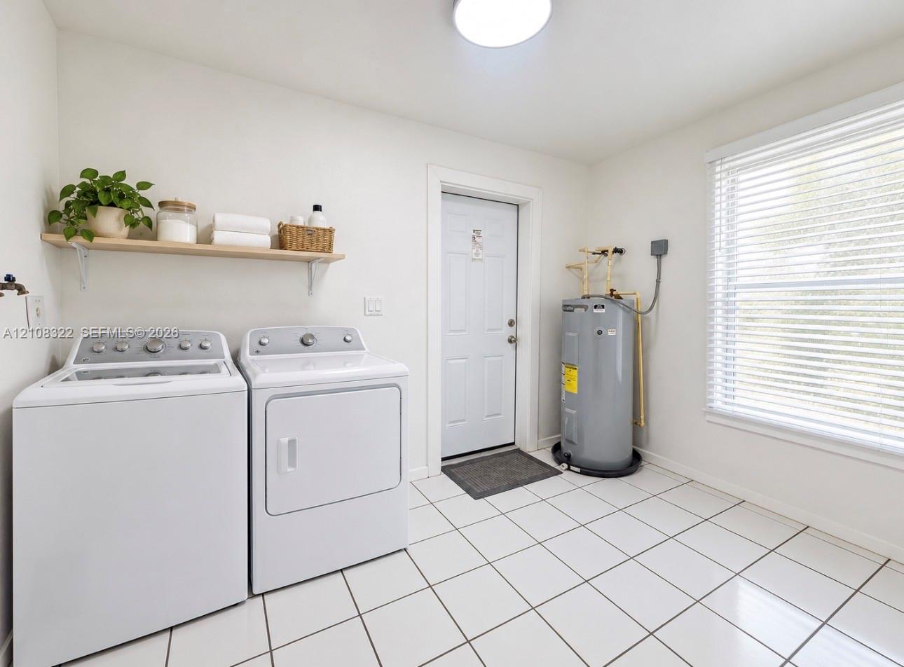 Utility space featuring white ceramic tile flooring, a window with horizontal blinds, a solid-panel exterior door, and a mounted wall shelf