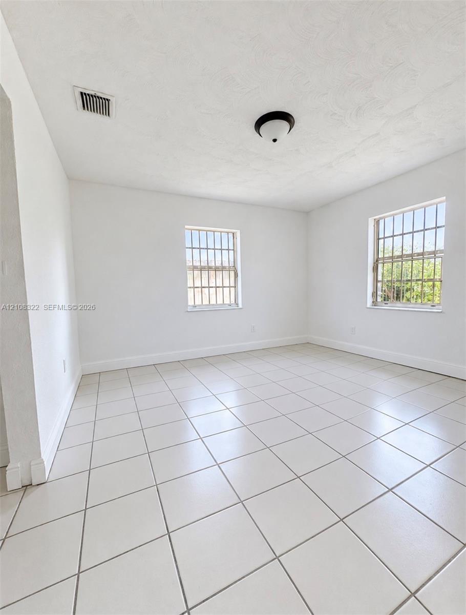 Neutral interior space featuring large-format ceramic tile flooring, two windows with metal security bars, and a central flush-mount ceiling fixture