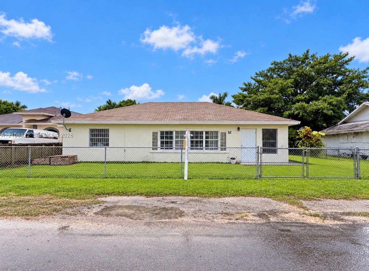 Single-story residence with a hipped roof, light-colored stucco exterior, multi-pane windows, and a chain-link fenced perimeter Single-story residence with a hipped roof, light-colored stucco exterior, multi-pane windows, and a chain-link fenced perimeter