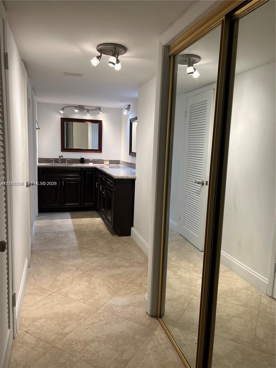 Dark-finish built-in vanity with a light-toned countertop, tile flooring, mirrored sliding closet doors, and multi-directional track lighting