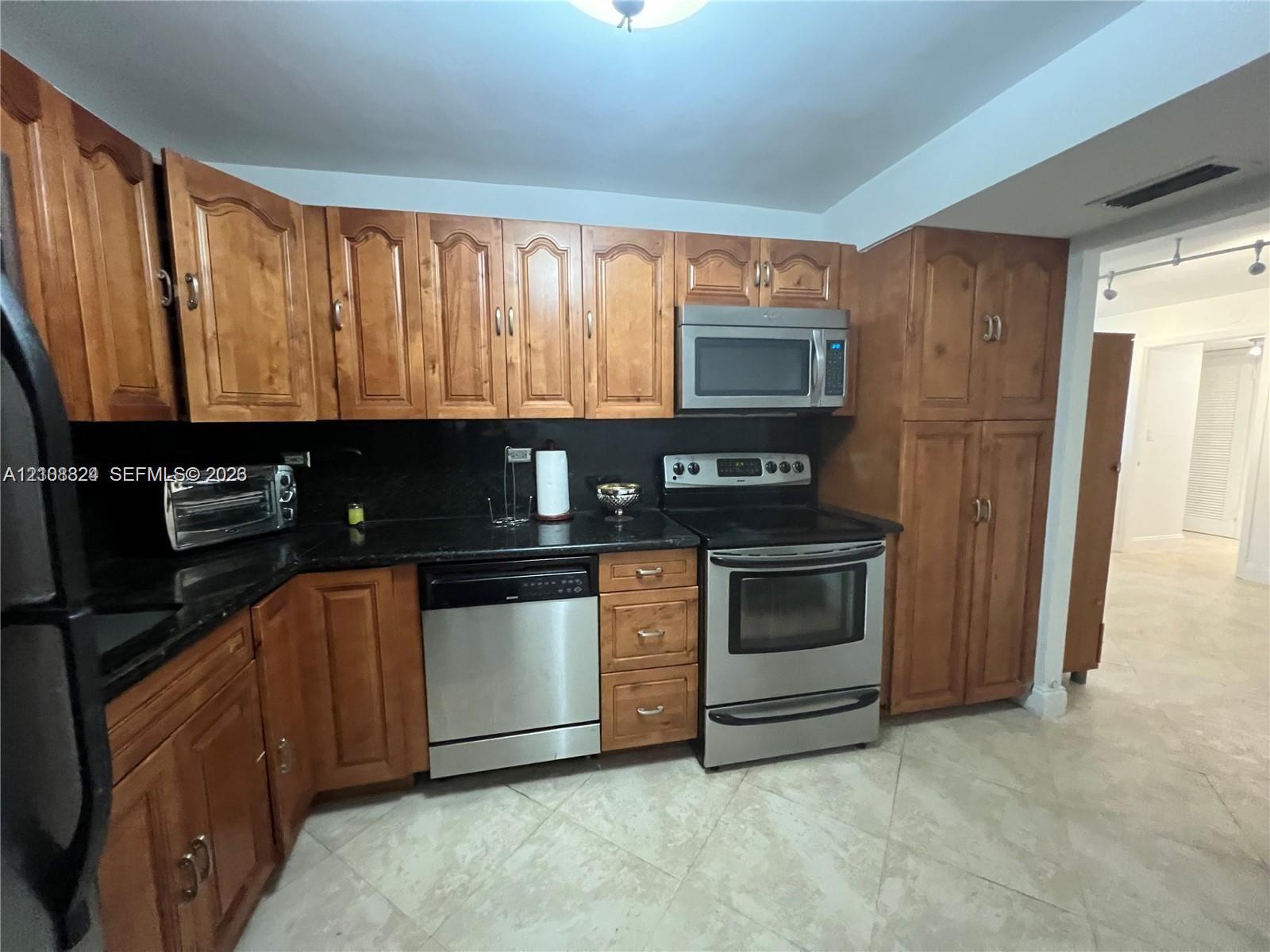 Kitchen featuring stained wood cabinetry, stone countertops, and stainless steel appliances including a built-in microwave, range, and dishwasher