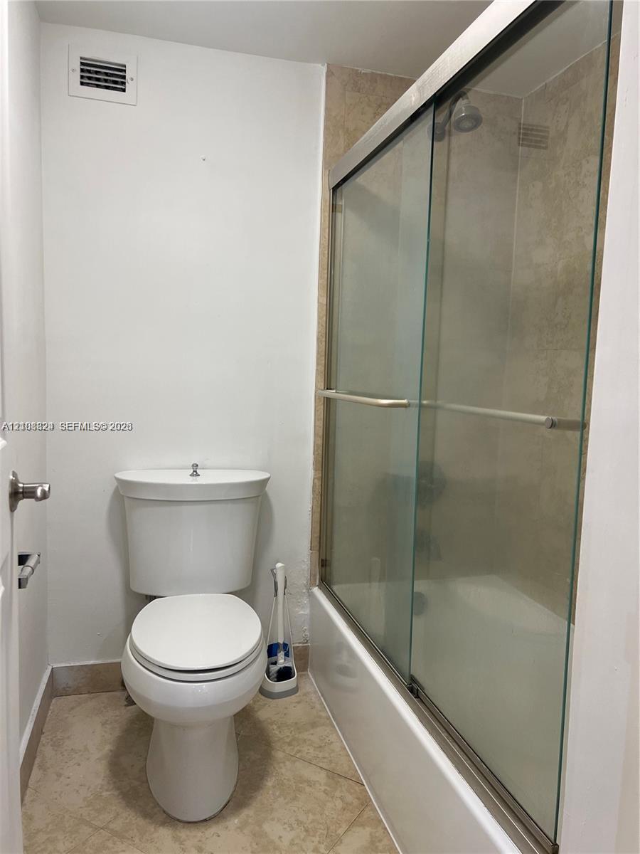 Full bathroom featuring a glass-enclosed shower, stone-finish tile flooring, neutral wall tile surround, and a standard porcelain toilet