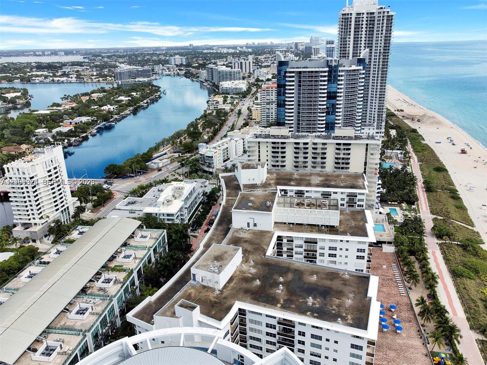 Aerial perspective of a multi-story coastal residential complex situated between the Atlantic Ocean and the Intracoastal Waterway, featuring expansive shoreline access, paved pedestrian paths, and proximity to regional maritime landmarks