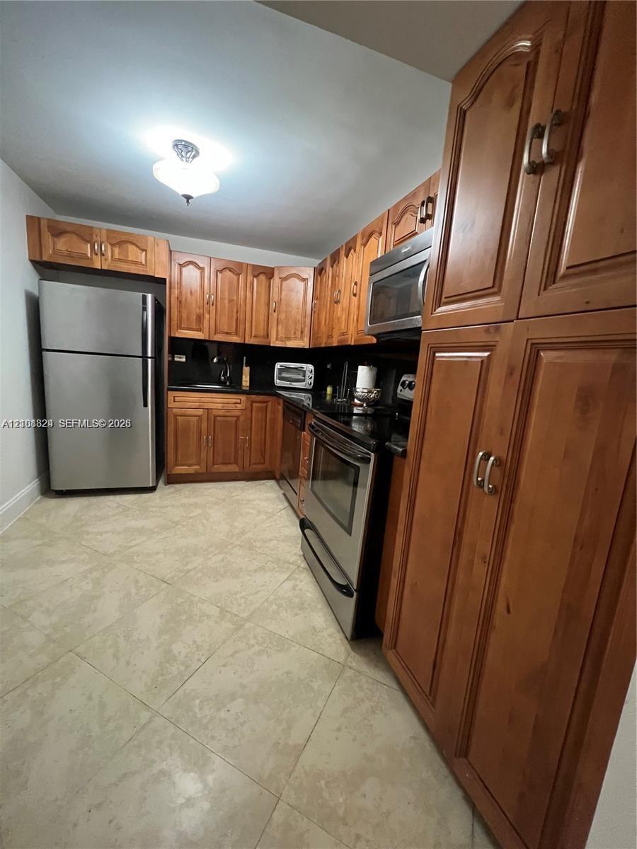 Kitchen featuring stained wood cabinetry, stainless steel appliances, dark stone countertops, and tile flooring
