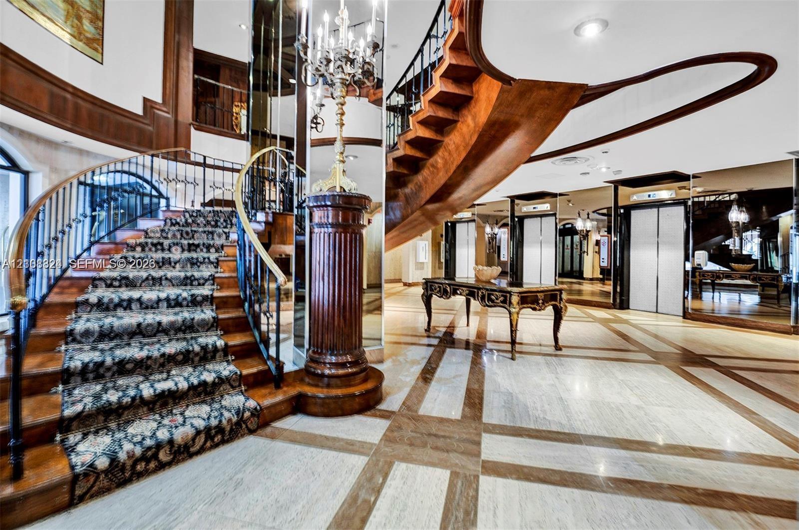 Grand foyer featuring a dual-tone stone floor, a sweeping staircase with custom metal railing, full-height wall mirrors, and recessed lighting