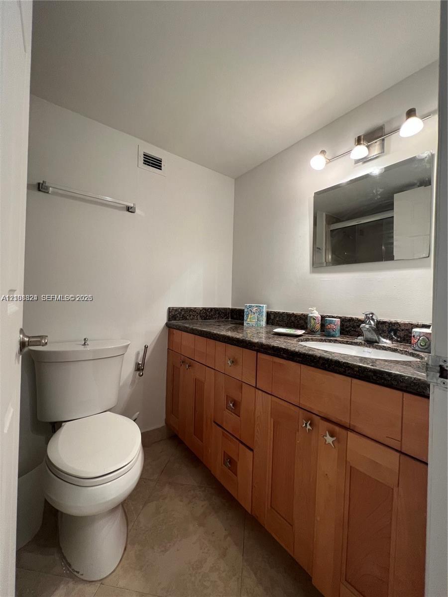Bathroom featuring a stone-surface vanity with an integrated oval sink, natural wood-finish cabinetry, a framed wall mirror, and tile flooring
