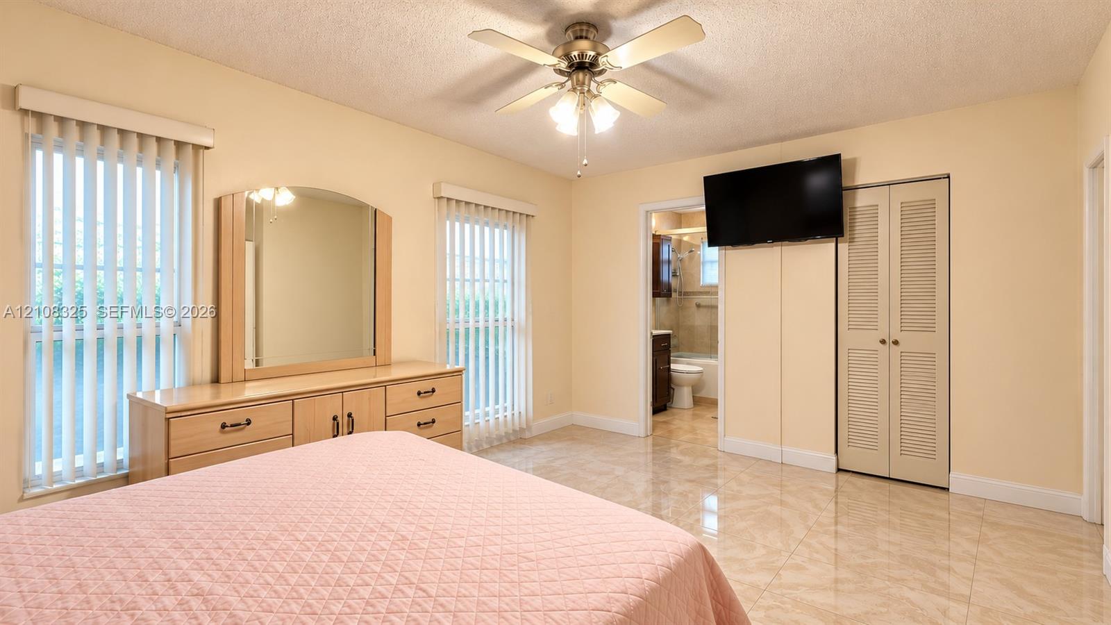 Room featuring ceramic tile flooring, dual windows with vertical blinds, a ceiling fan with integrated lighting, and a closet with louvered doors