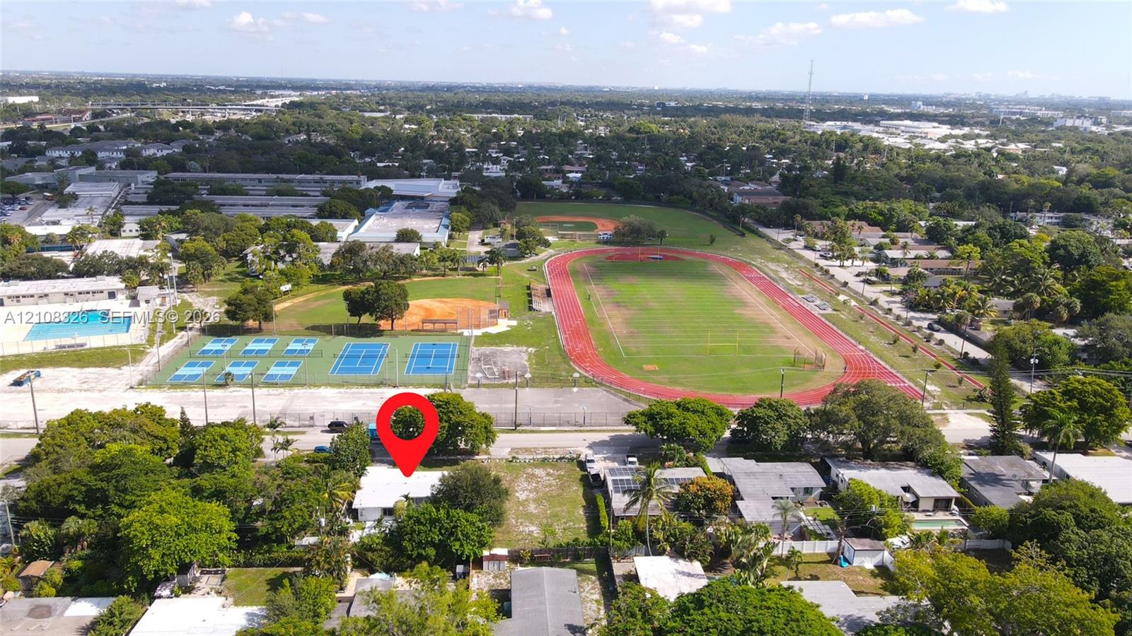 Aerial perspective of residential property featuring mature landscaping and proximity to public recreational facilities including tennis courts and an athletic track