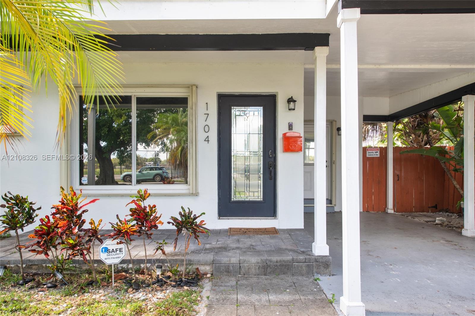 Exterior facade featuring a covered carport, a dark-toned front entry door with a decorative glass insert, a large picture window, and stone-tile porch surfacing