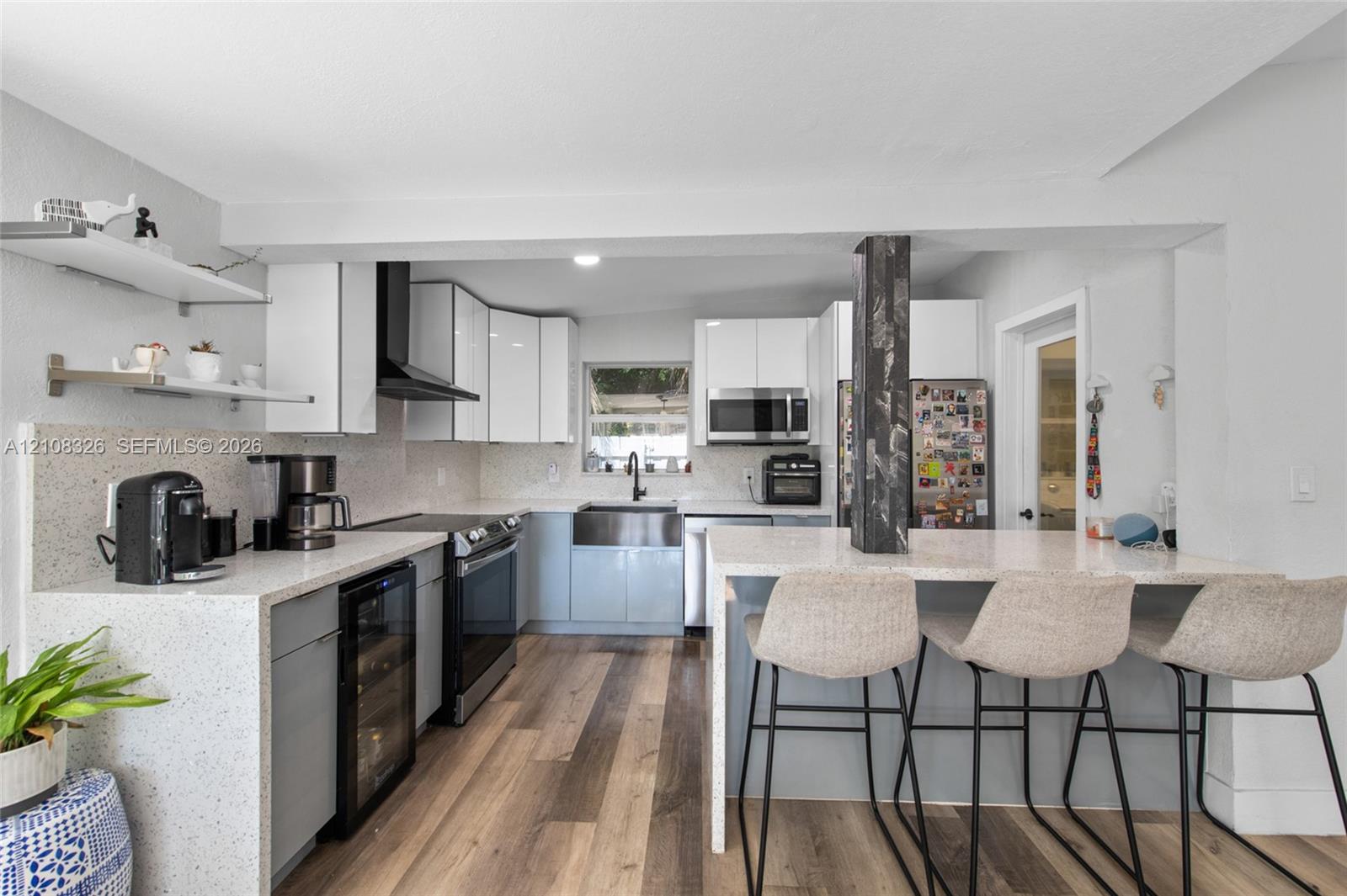 Kitchen featuring flat-panel cabinetry, quartz countertops with waterfall edge, apron-front stainless steel sink, built-in beverage refrigerator, and wood-finish flooring Kitchen featuring flat-panel cabinetry, quartz countertops with waterfall edge, apron-front stainless steel sink, built-in beverage refrigerator, and wood-finish flooring