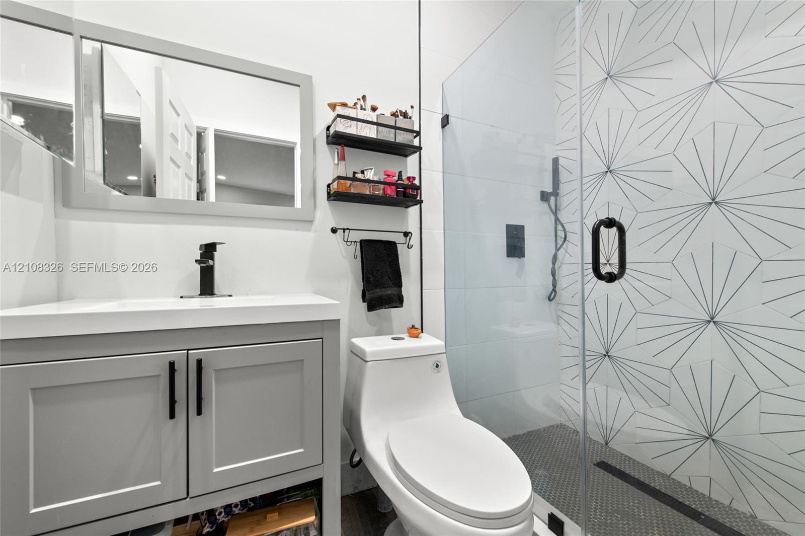 Bathroom featuring a grey vanity with a rectangular sink, matte black faucet, glass-enclosed shower with geometric patterned tile, and a modern one-piece toilet Bathroom featuring a grey vanity with a rectangular sink, matte black faucet, glass-enclosed shower with geometric patterned tile, and a modern one-piece toilet