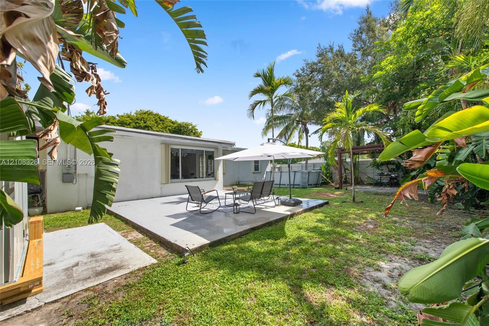 Rear exterior featuring a concrete patio, grassy yard, and mature landscaping