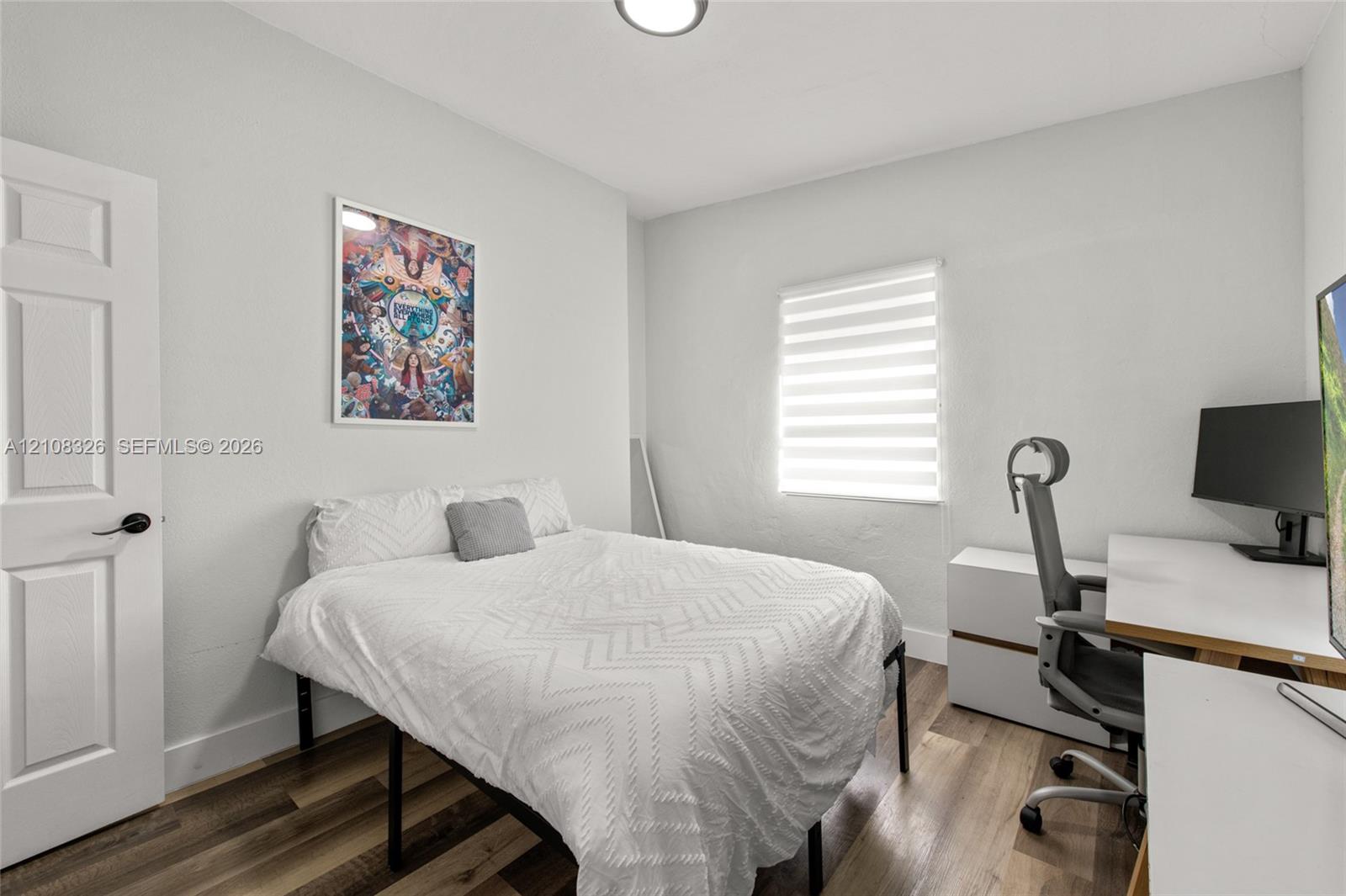 Room featuring wood-finish flooring, a multi-panel door with matte black hardware, and a window with integrated light-filtering shade