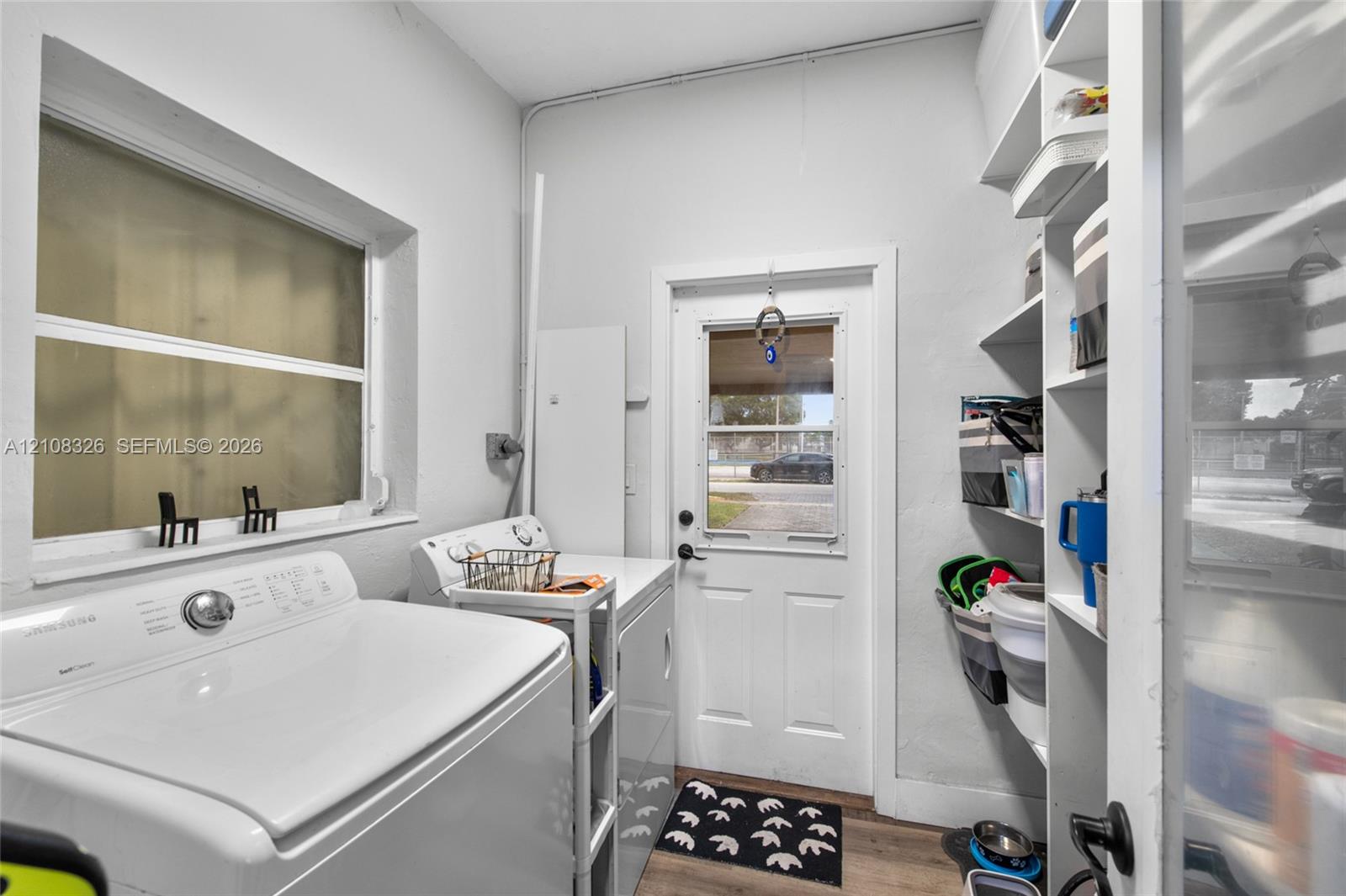 Laundry area featuring wood-finish flooring, white built-in shelving, and a glass-paneled exterior door Laundry area featuring wood-finish flooring, white built-in shelving, and a glass-paneled exterior door