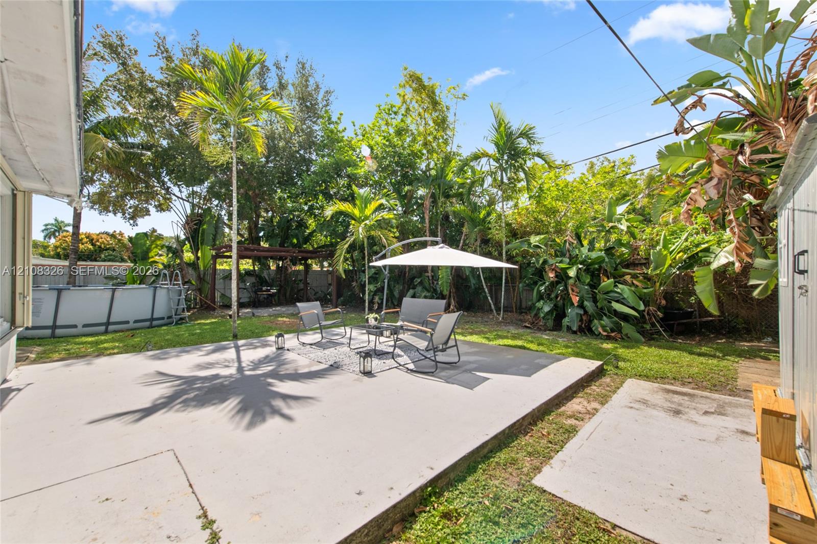 Expansive backyard featuring a concrete patio, mature palm trees, perimeter fencing, and an above-ground pool