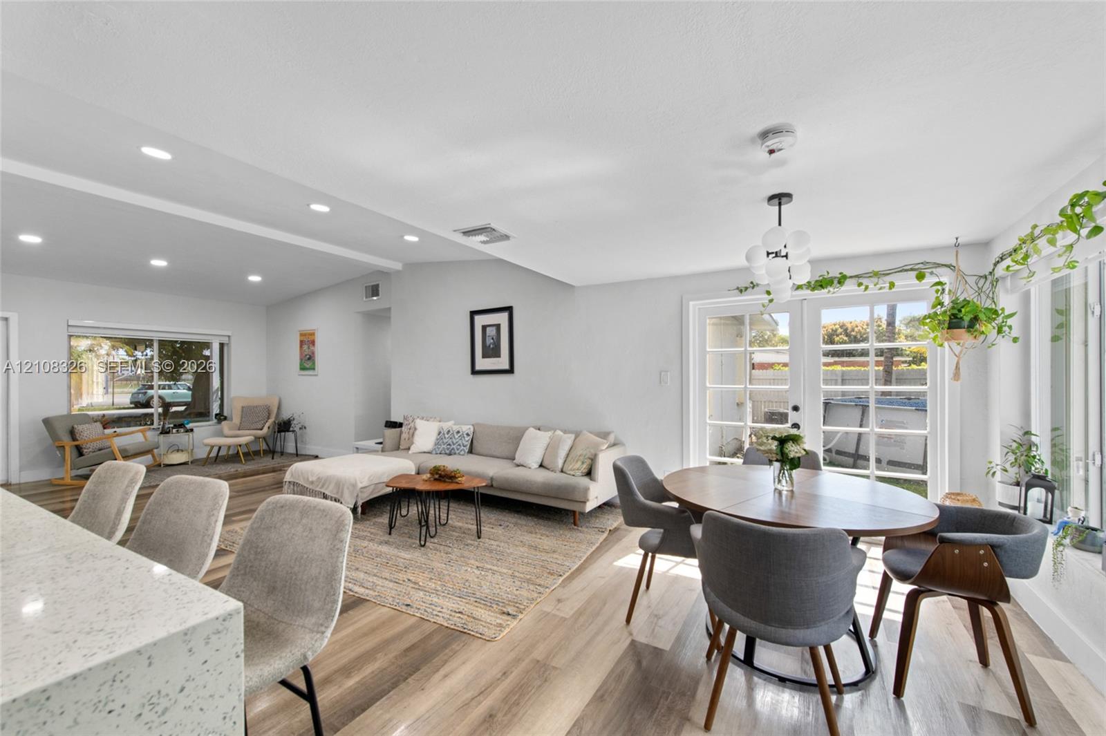 Open-concept interior featuring wood-finish flooring, recessed lighting, a modern multi-globe chandelier, and double French doors providing exterior access Open-concept interior featuring wood-finish flooring, recessed lighting, a modern multi-globe chandelier, and double French doors providing exterior access