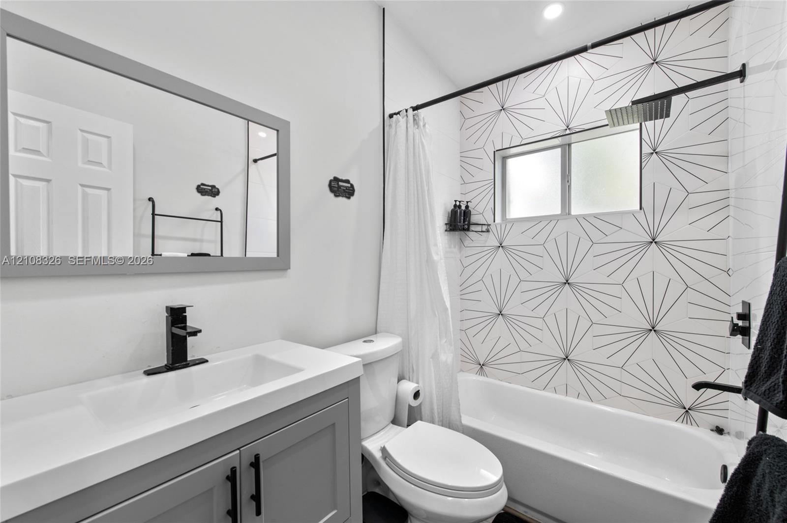 Bathroom featuring a vanity with a rectangular sink, matte black faucet, gray cabinetry, and geometric patterned tile shower surround with a rain-style shower head