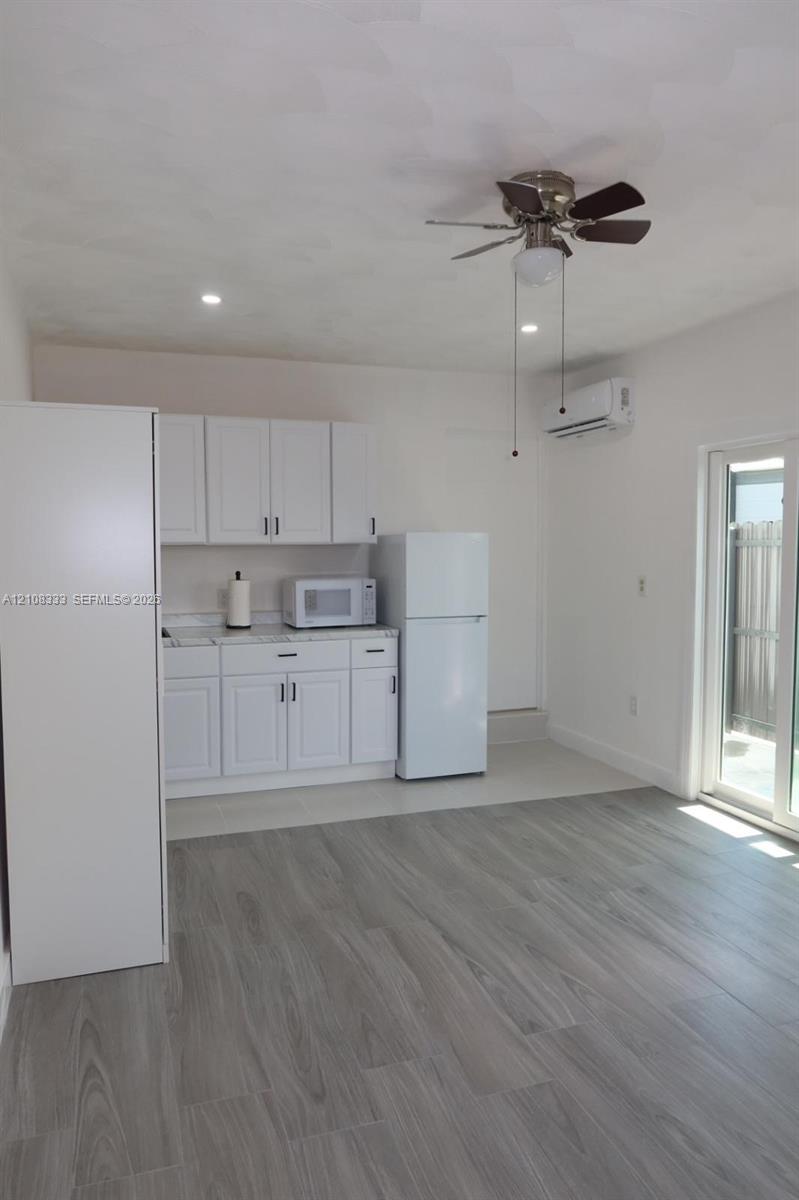 Kitchenette featuring white shaker-style cabinetry, stone-finish countertops, wood-finish flooring, a wall-mounted climate control unit, and a sliding glass door