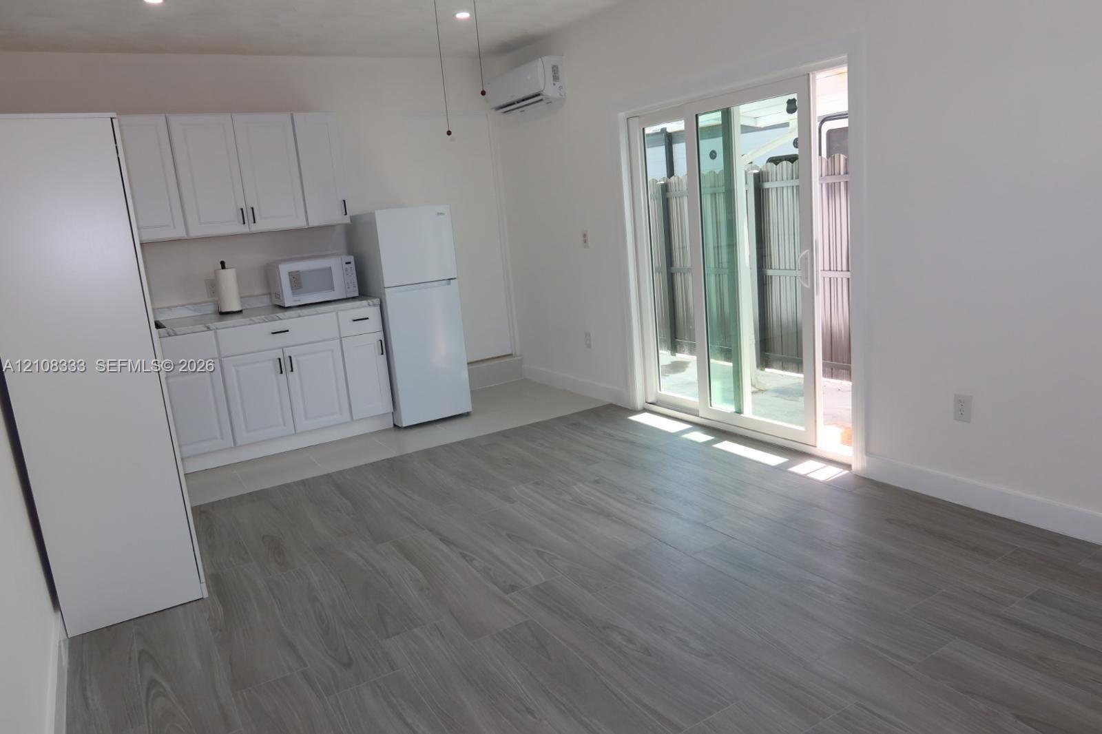 White cabinetry, wood-finish flooring, wall-mounted mini-split HVAC unit, and glass sliding doors