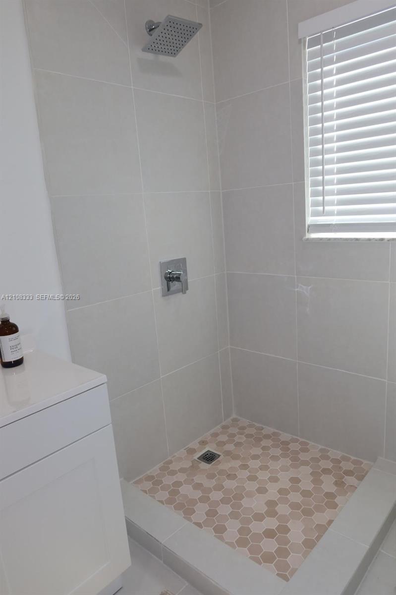 Walk-in shower featuring large-format wall tile, hexagonal floor tiling, a square rainfall showerhead, and a single-handle chrome fixture