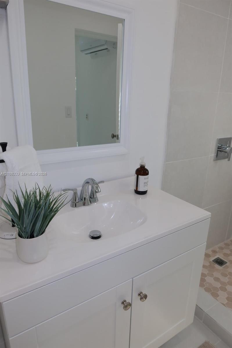 White vanity with a rectangular countertop, integrated basin, chrome faucet, and framed wall mirror, complemented by a walk-in shower with large-format wall tile and hexagonal floor tile