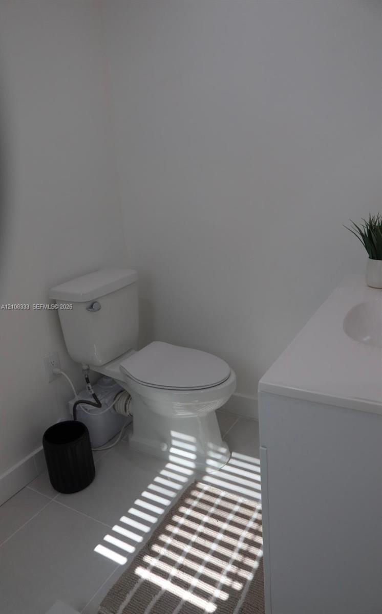 White ceramic toilet and modern vanity with a white countertop and integrated sink, set against neutral tile flooring