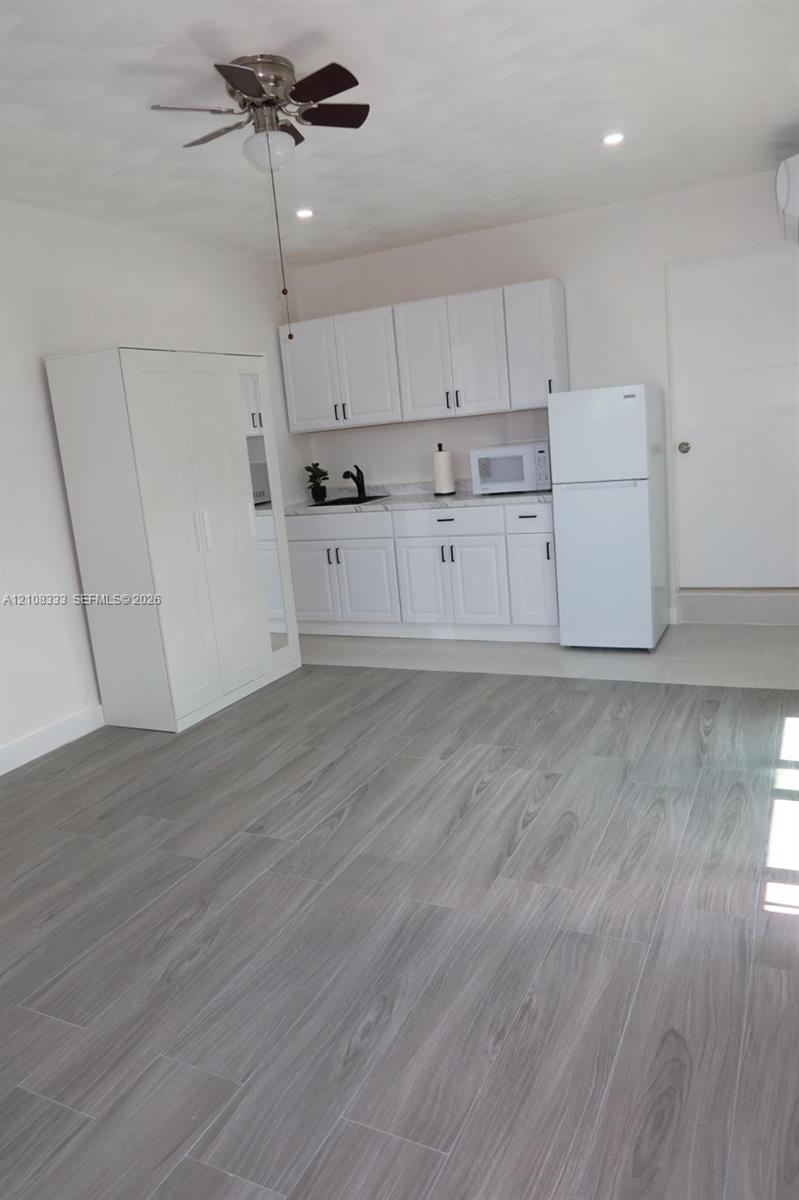 Kitchenette featuring white cabinetry, wood-finish tile flooring, a matte black faucet, and a ceiling fan with integrated lighting
