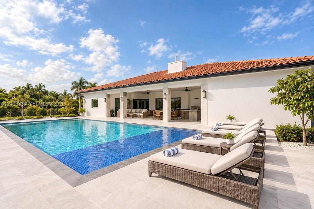 Outdoor living area featuring a covered lanai with stone pillars, an inground pool with tile border, and expansive stone-finish decking