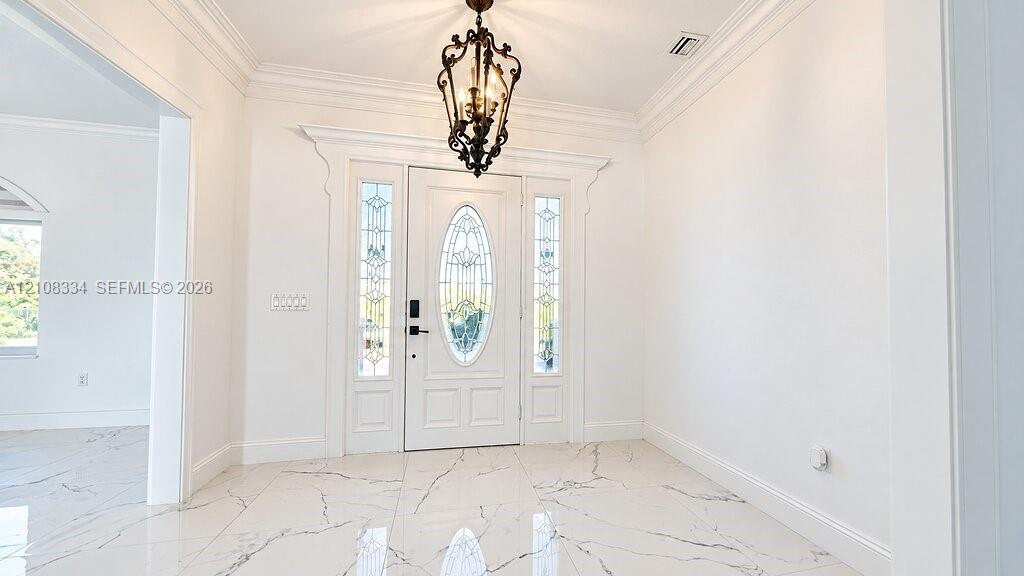 Foyer featuring large-format tile flooring with marble-style veining, crown molding, iron lantern-style pendant lighting, and a white front entry door with a decorative oval glass inlay flanked by sidelights