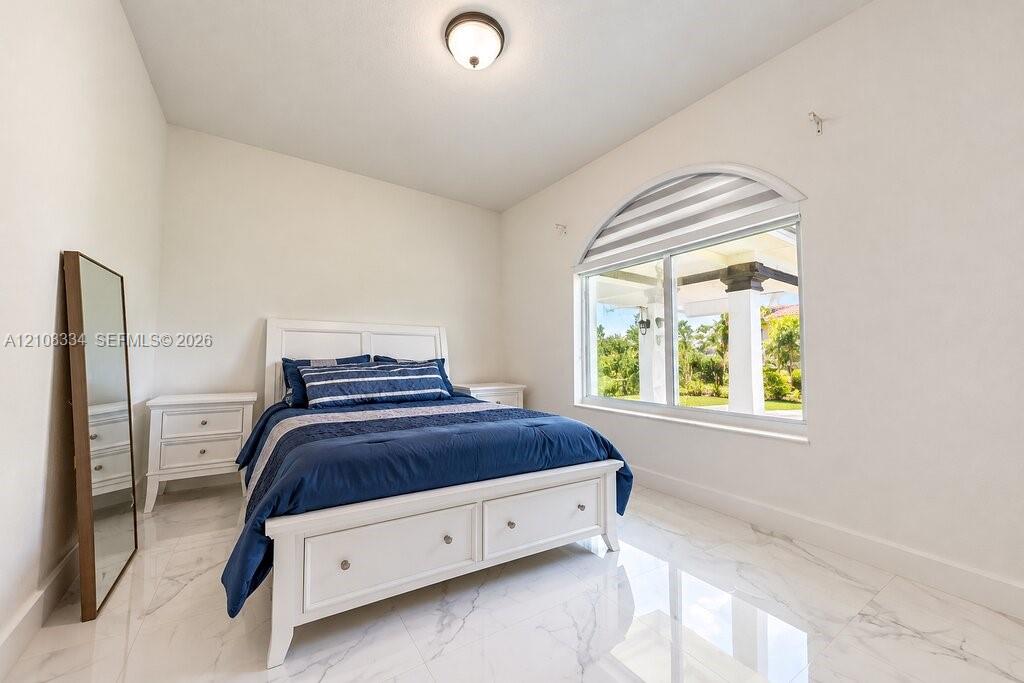 Large room featuring polished stone-finish flooring, an arched window with integrated shading, and a centered flush-mount light fixture