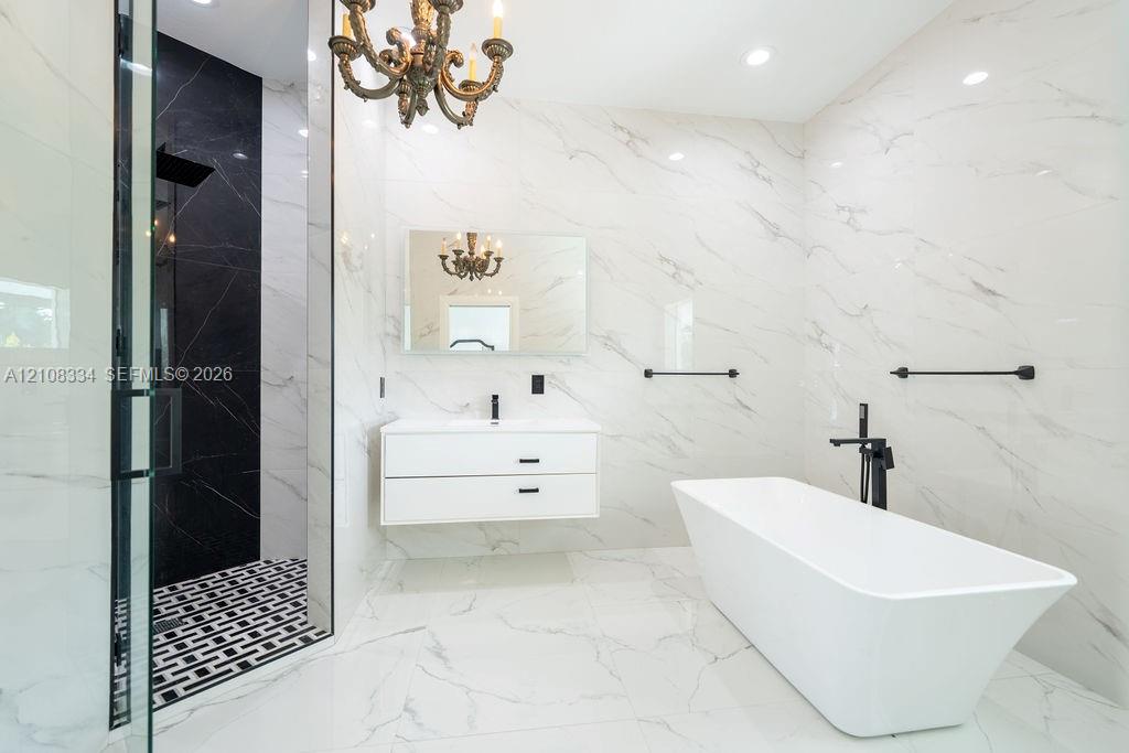 Bathroom featuring large-format veined tile, floating double-drawer vanity, freestanding soaking tub with matte black floor-mounted faucet, and glass-enclosed shower with contrasting tile inlay