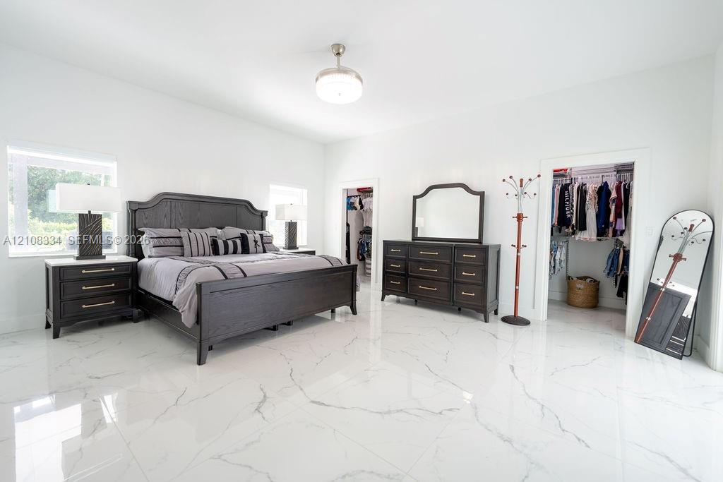 Polished stone-finish flooring with vein detailing, dual walk-in closets with built-in shelving, and a modern central ceiling-mounted light fixture