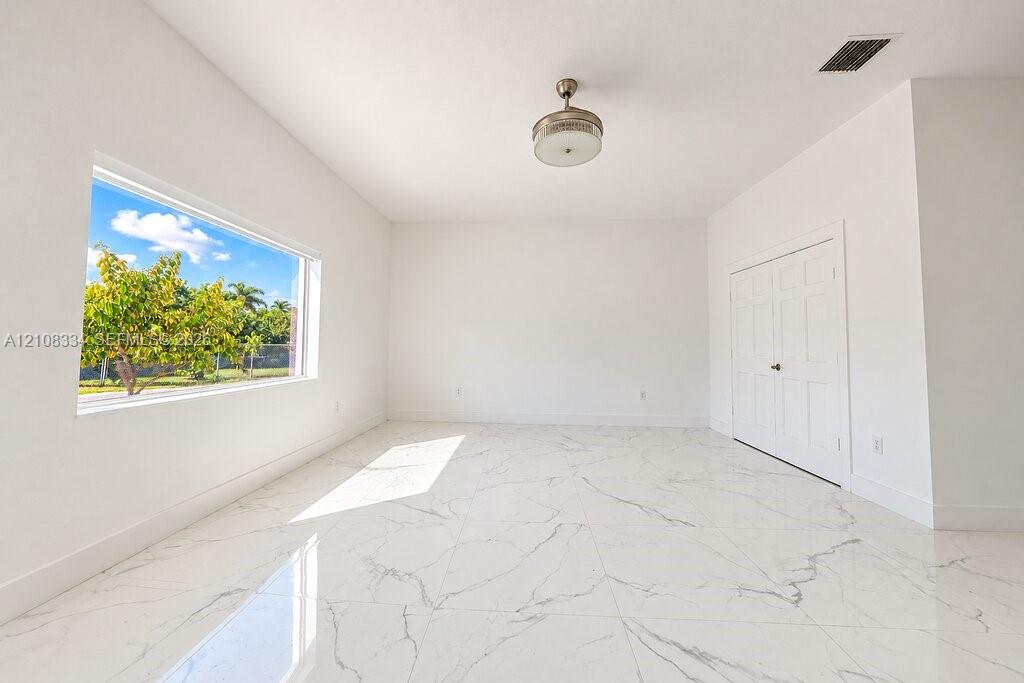Interior space featuring polished white-veined tile flooring, large rectangular window, dual-panel closet doors, and central ceiling-mounted light fixture