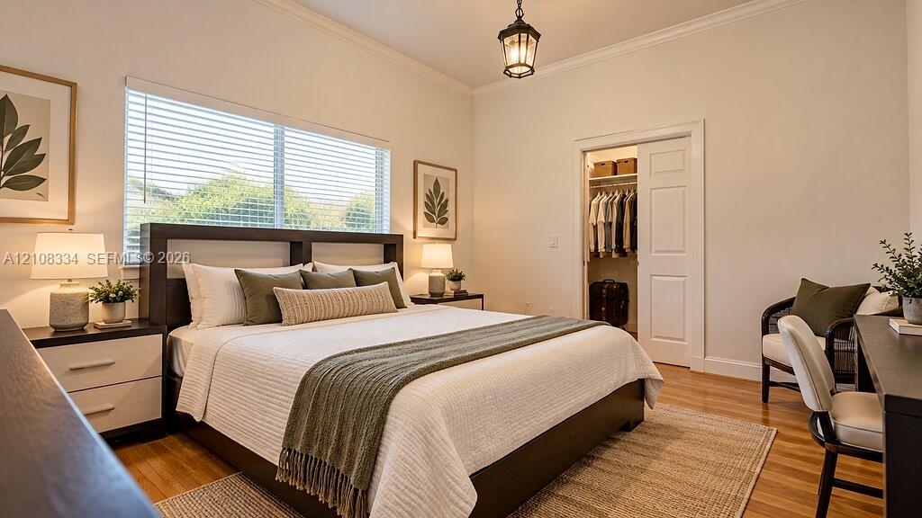 Bedroom featuring wood-finish flooring, crown molding, a hanging lantern-style light fixture, and a reach-in closet with a paneled door
