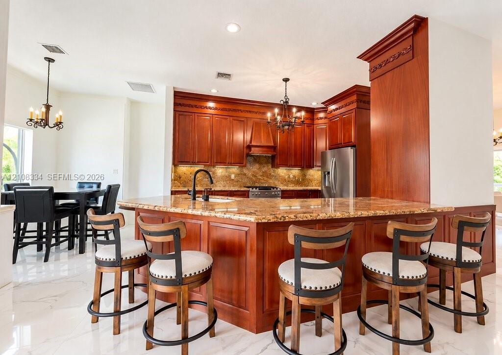 Kitchen featuring raised-panel wood cabinetry with crown molding, stone countertops, a multi-tiered central island, built-in stainless steel appliances, and polished tile flooring