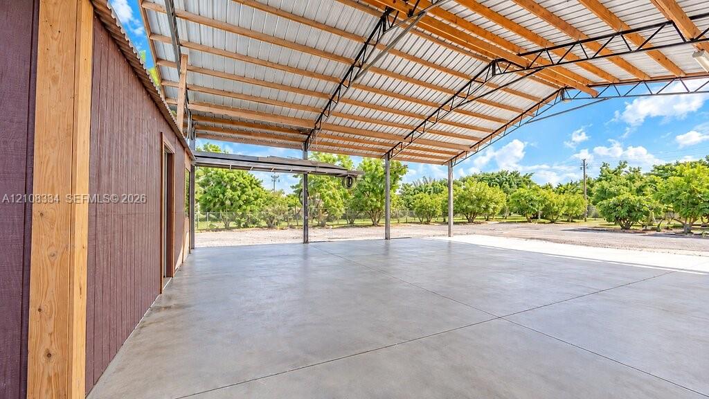 Covered outdoor workspace featuring a concrete foundation, exposed wooden truss ceiling, and metal roofing