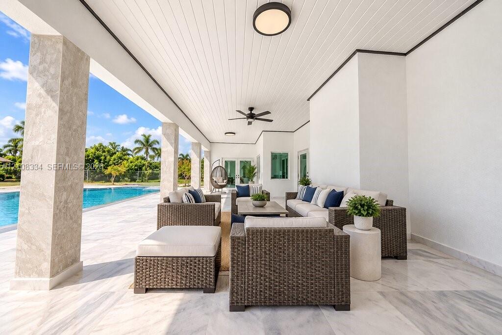 Covered outdoor patio featuring stone-tiled flooring, beadboard ceiling, recessed lighting, ceiling fans, and stone-finished structural pillars