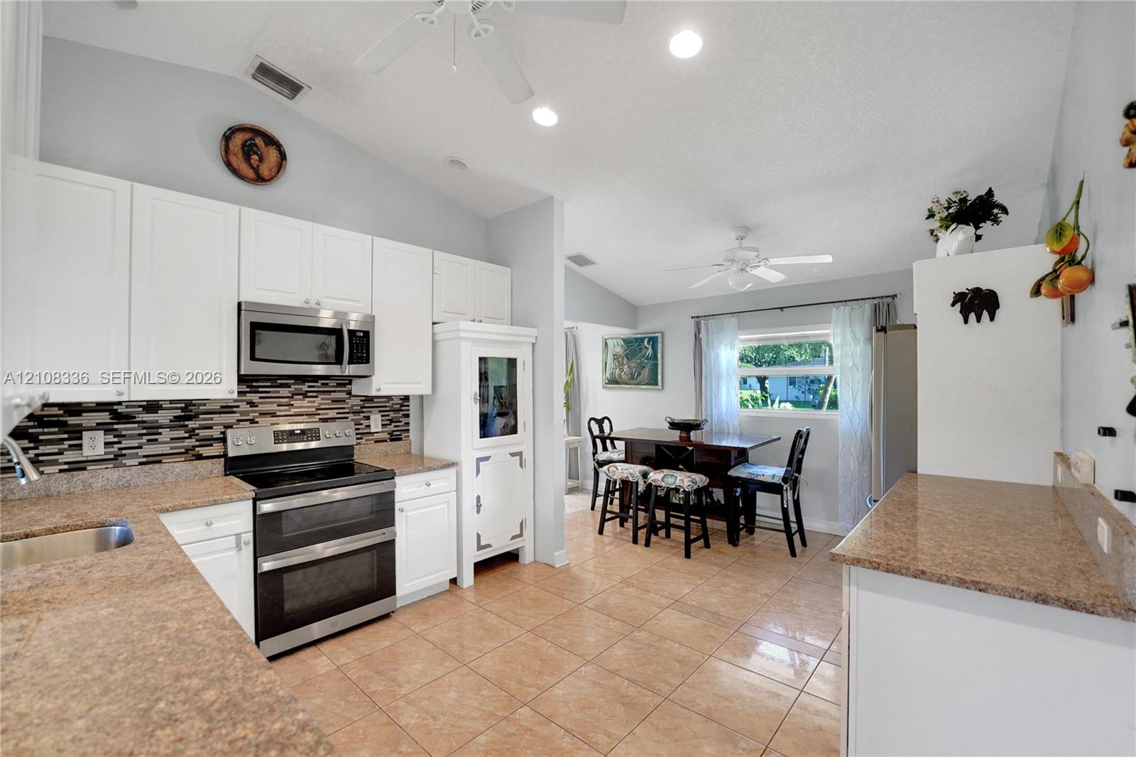 Kitchen featuring white cabinetry, stone-finish countertops, stainless steel appliances, multi-toned mosaic tile backsplash, and ceramic tile flooring