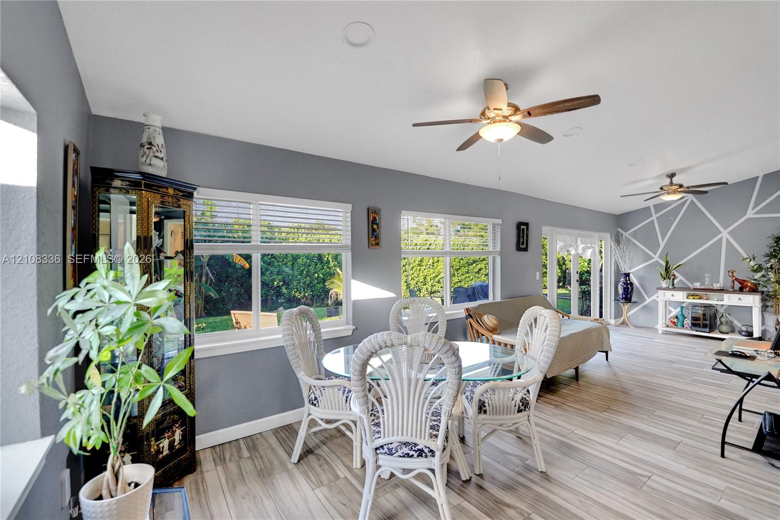 Open-concept room featuring wood-finish flooring, recessed lighting, dual ceiling fans, geometric wall detailing, and expansive windows