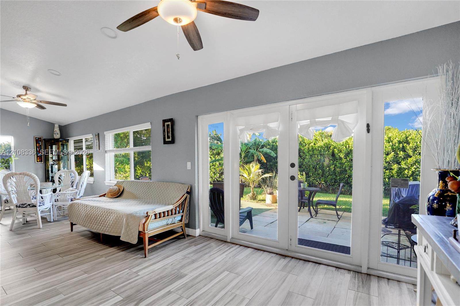 Living area featuring wood-finish tile flooring, recessed lighting, dual ceiling fans, and multi-panel glass doors opening to a stone-paved patio