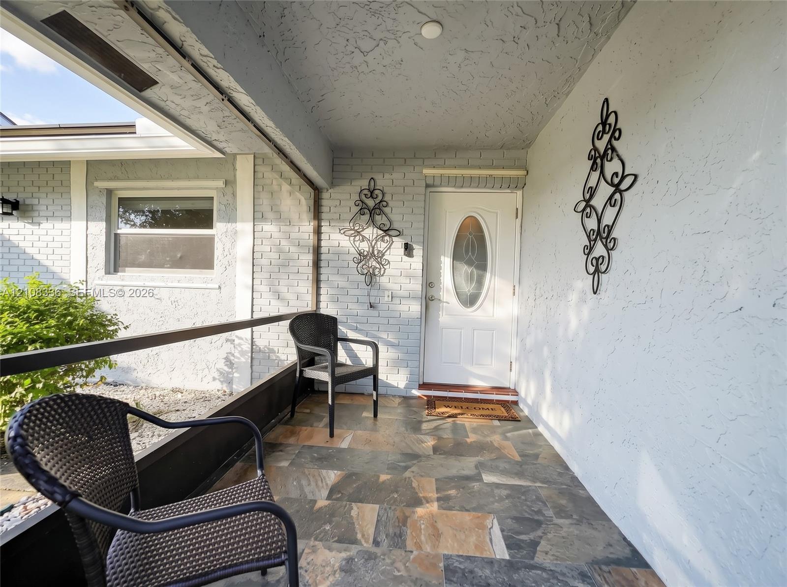 Covered entryway featuring painted brick walls, multi-tonal stone flooring, and a glass-paneled entry door