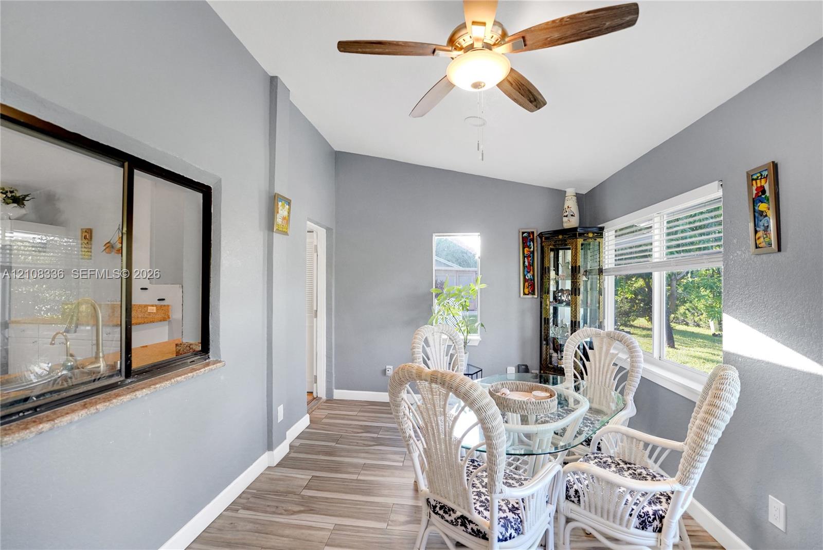Vaulted ceilings featuring a centrally mounted ceiling fan, wood-finish tile flooring, a horizontal interior service window with a stone-finish ledge, and large windows providing natural light