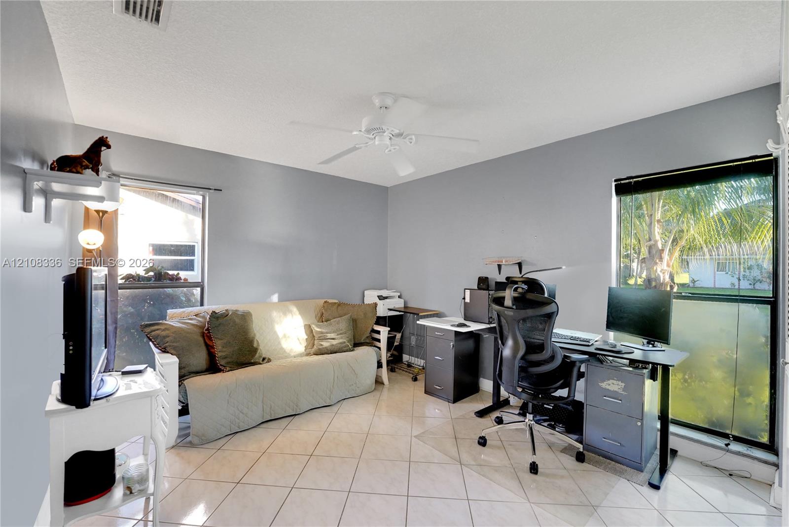 Neutral-toned interior featuring diagonal tile flooring, dual windows, a ceiling fan, and a wall-mounted shelving unit
