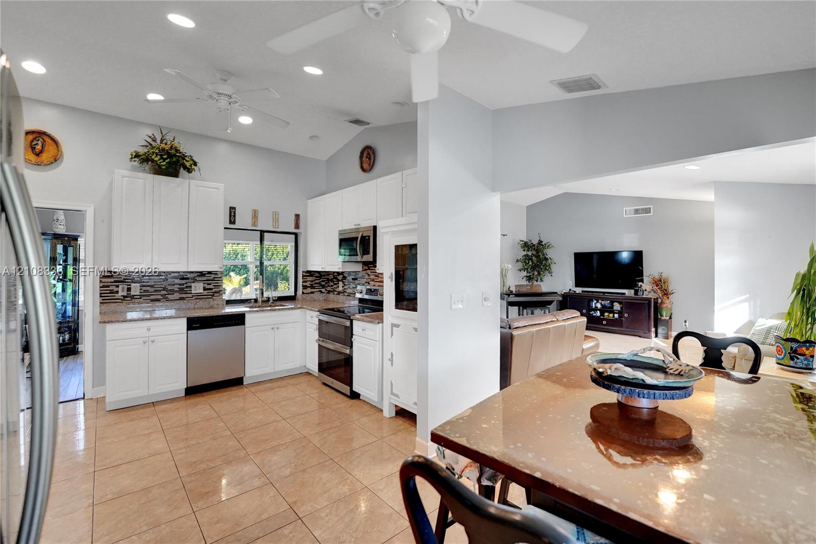 Kitchen featuring white cabinetry, stone-finish countertops, stainless steel appliances, a multi-tone decorative backsplash, and ceramic tile flooring under a vaulted ceiling