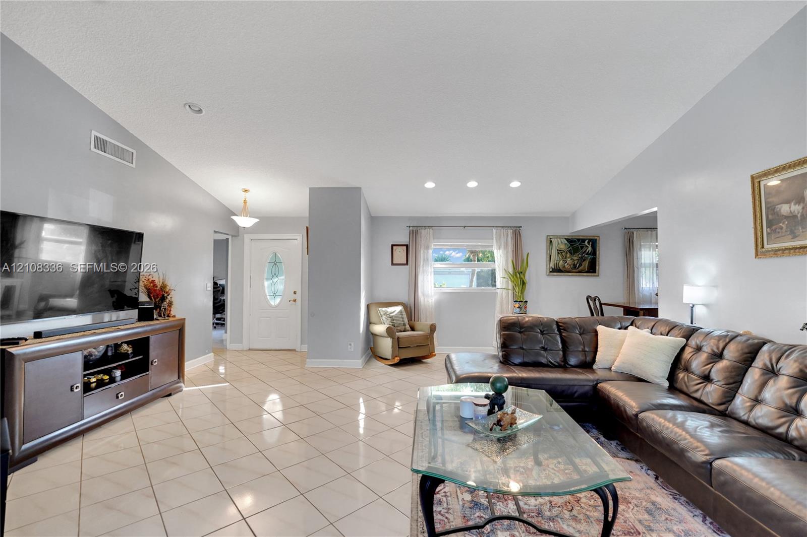 Open-concept living space featuring vaulted ceilings, light-toned ceramic tile flooring, recessed lighting, and a white entry door with an oval glass insert